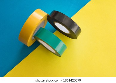 Set Of Multicolored Rolls Of Electrical Round Adhesive Sticky Insulation Tape Roll On Blue And Yellow Background.