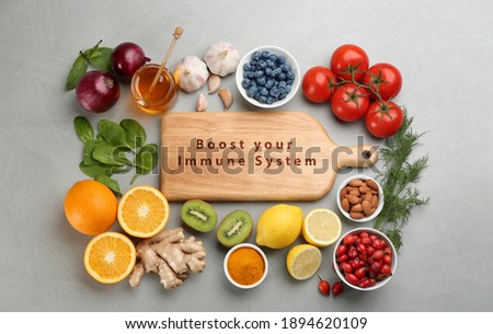 Set of natural products and wooden board with text Boost Your Immune System on grey table, flat lay