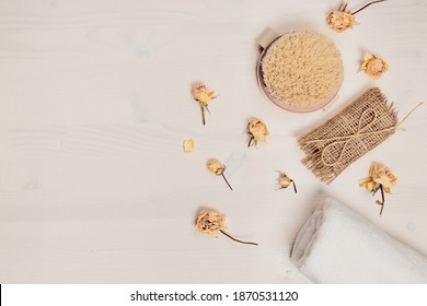 Set Of Natural Soap, Aroma Oil, White Towel And Body Brush With Dried Rose Buds As A Decoration On Wooden Background. Home Spa Concept. Beauty Rituals Theme.