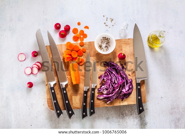 набор новых профессиональных кухонных ножей на деревянной разделочной доске и овощами