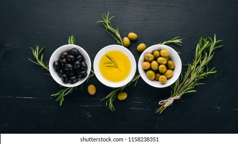 A set of olives and olive oil and rosemary. Green olives and black olives. On a black wooden background. Free space for text.