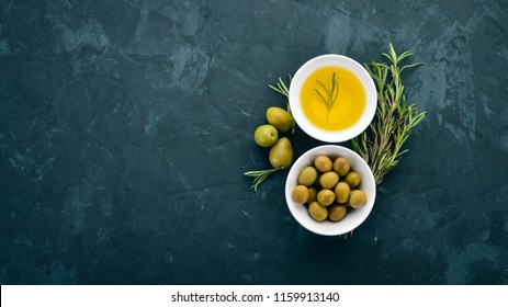 A set of olives and olive oil and rosemary. Green olives and black olives. On a black stone background. Free space for text.
