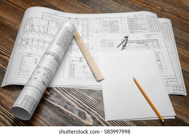 A set of open and rolled up blueprints on wooden table background with a pencil, a ruler and compasses lying beside. Engineering and design. Construction projects. Planning.