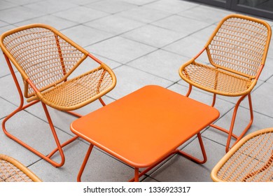 Set Of Orange Patio Furniture Around A Metal Coffee Table, In A Modern Backyard Scene With Space For Text On Top