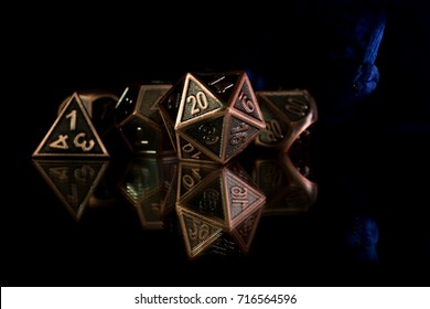 A set of polyhedral dice  with a blue drawstring bag on a mirrored surface. These dice are used for role playing games.