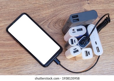 Set of power banks with a telephone on a wooden table. A portable charger charges a smartphone with a white screen mockup