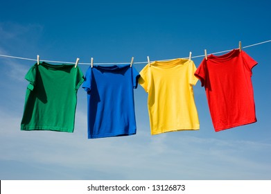 A Set Of Primary Colored T-shirts Hanging On A Clothesline On A Beautiful, Sunny Day, Add Text Or Graphic To Shirts Or Copy Space