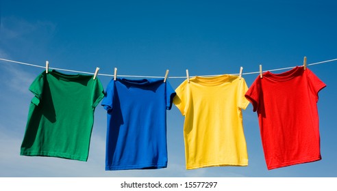 A Set Of Primary Colored T-shirts Hanging On A Clothesline On A Beautiful, Sunny Day, Add Text Or Graphic To Shirts Or Copy Space