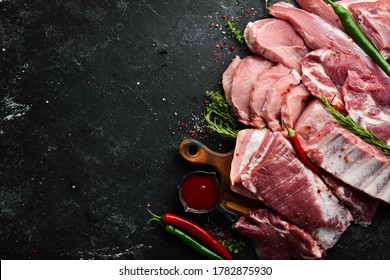 Set of raw meat. Pork meat on black stone background with spices and herbs. Top view. Rustic style.