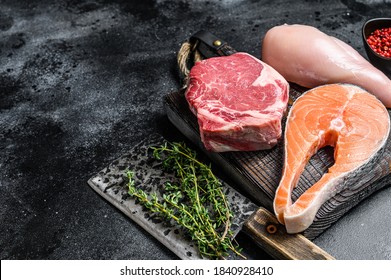 Set of raw meat steaks salmon, beef and chicken on a cutting board. Black background. Top view. Copy space
