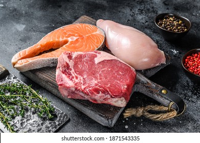 Set of raw meat steaks salmon, beef and chicken on a cutting board. Black background. Top view