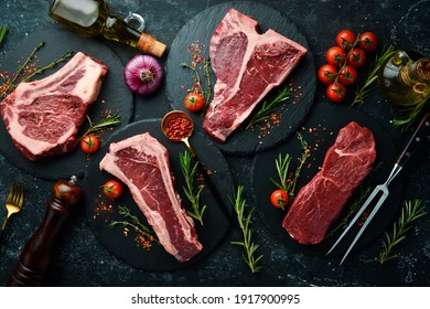 Set of raw steaks - t-bone, tomahawk, striploin, tenderloin, new york steak. On a black stone background. Top view.