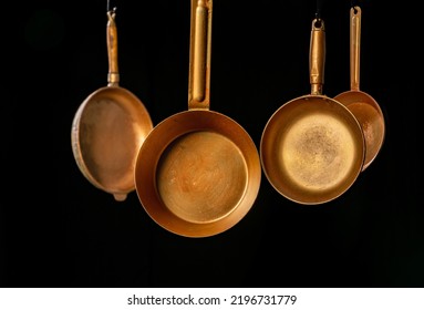 Set rustic copper fryingpans hanging on isolated black studio background. Round empty gold pans with handles. Kitchenware, utensils for cooking and frying. Restaurant interior background.