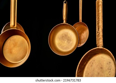 Set rustic copper fryingpans hanging on isolated black studio background. Round empty gold pans with handles. Kitchenware, utensils for cooking and frying. Restaurant interior background.