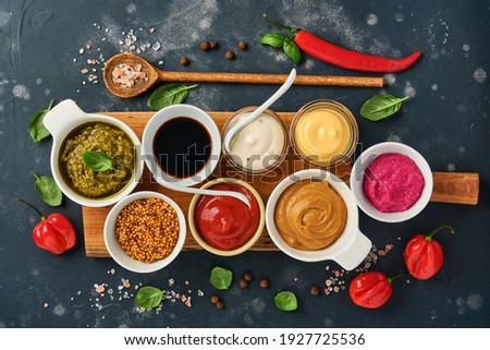 Set of sauces in bowls - ketchup, mayonnaise, mustard, soy sauce, bbq sauce, pesto, chimichurri, mustard grains on dark stone background. Top view copy space.