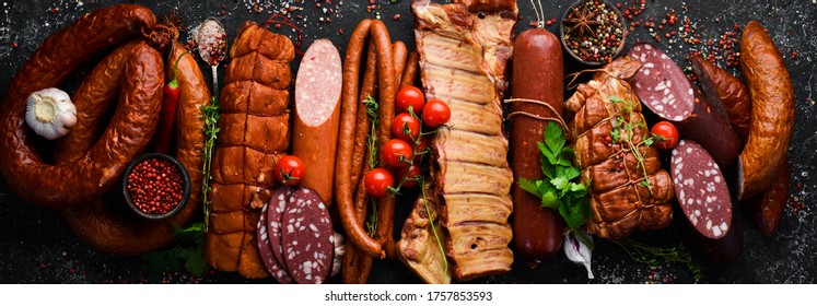 Set of sausage, salami and smoked meat with rosemary and spices on a black stone background. Top view. Free space for text.