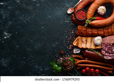 Set of sausage, salami and smoked meat with rosemary and spices on a black stone background. Top view. Free space for text.