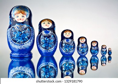 A Set Of Seven Blue Painted Russian Nesting Dolls On Mirror Surface. Creative Concept Photo Of Set Of Seven Blue Painted National Toys Russian Nesting Dolls On Mirror Surface.