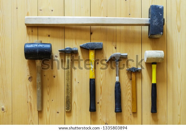 Set of seven old used\
hammers of different purposes, sizes and colors on wooden plank\
floor background