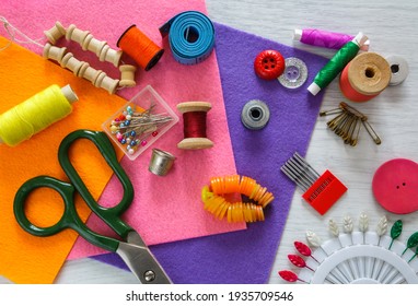 A Set Of Sewing Accessories. Sewing Accessories For Sewing: Orange Fabric, Thimbles, Spools Of Thread, Tailor's Scissors, A Set Of Pins And A Tape Measure On A Gray Wooden Table. View From Above
