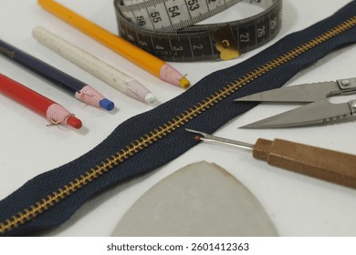 A set of sewing tools including thread, sewing meter, thread cutter, pins, fabric chalk with white background, close-up photo.