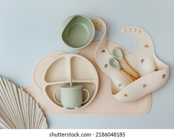 Set Of Silicone Dishware And Baby Accessories On Blue Light Background, Flat Lay