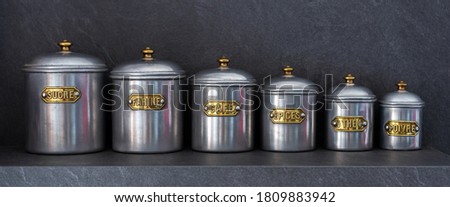 Set of six pewter jars of different sizes with their lids lined up on a shelf and bearing the inscriptions 