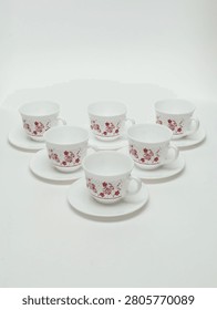 Set of six white ceramic teacups and saucers with red floral pattern isolated on white background.