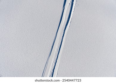 A set of ski tracks forming a pattern in fresh, untouched off-piste snow, highlighting the thrill of off-trail skiing and winter exploration.