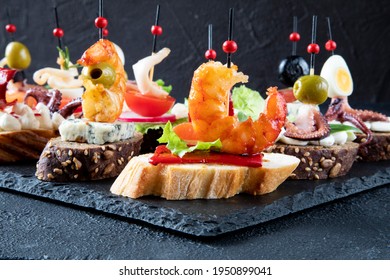 A set of Spanish tapas - a backdrop of traditional Spanish seafood sandwiches. In the foreground, tapas with fried shrimp, red pepper, and green lettuce