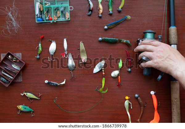 set of spinnings. A\
spinning coil and a set of different baits for catching predatory\
fish are laid out on a brown table. The fisherman\'s hand takes the\
spinning\
