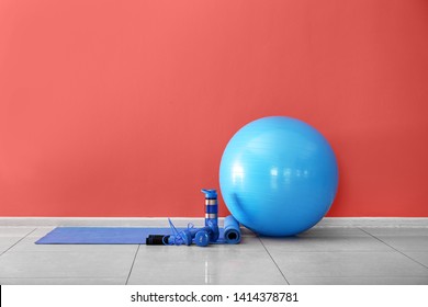 Set Of Sports Equipment With Fitness Ball And Bottle Of Water Near Color Wall