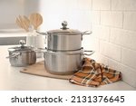 Set of stainless steel cookware and kitchen utensils on table near white brick wall