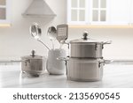 Set of stainless steel cookware and kitchen utensils on white table indoors
