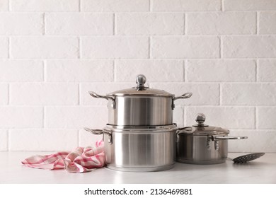 Set Of Stainless Steel Cookware On Table Near White Brick Wall