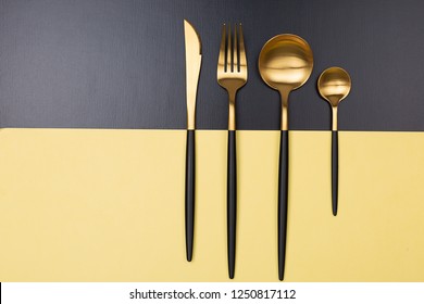 Set of stylish black and gold cutlery on color block background. Dark and moody vibes. Fashionable and luxury eating. Flat-lay, top view. Copy space for your text.