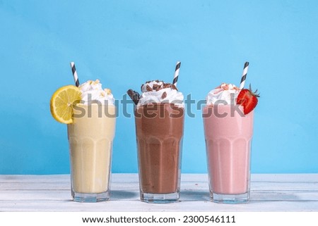 Set of summer refreshing milkshakes or smoothies with classic delicious taste - vanilla lemon, strawberry, chocolate, with whipped cream and toppings, On a white wooden light blue sunny background 