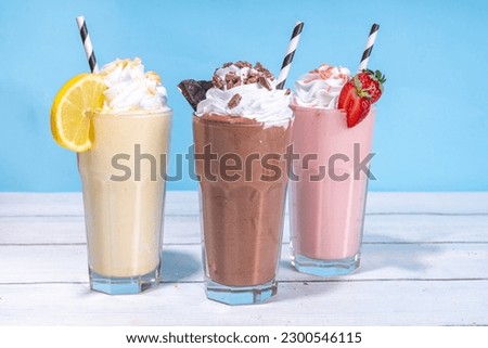 Set of summer refreshing milkshakes or smoothies with classic delicious taste - vanilla lemon, strawberry, chocolate, with whipped cream and toppings, On a white wooden light blue sunny background 