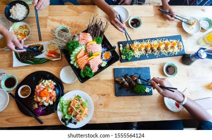 A set of sushi on a wooden table in a Japanese restaurant.Fresh salmon sliced for sushi menu.Party of friends or family eating sushi using bamboo sticks.