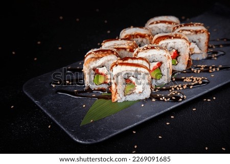 Set of sushi rolls dragon on a black matte plate.
Japanese traditional sushi dish with avocado, eel and soy sauce. A beautiful dish for an Asian restaurant menu.
