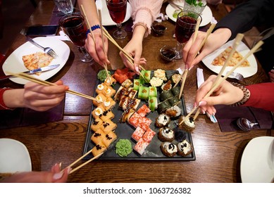 Un juego de rollos de sushi sobre una mesa en un restaurante. Una fiesta de amigos comiendo rollos de sushi usando palos de bambú.