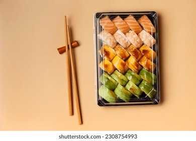 A set of sushi rolls in takeaway plastic packages with Chinese chopsticks on a light background, top view. Delivery of sushi in a plastic container - Powered by Shutterstock