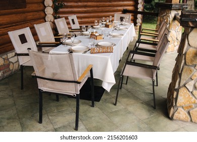 Set The Table On The Terrace With A Wooden Plate Reserved. Table Setting, Beautiful White Plates, Silver Cutlery And Crystal Glasses. Outdoor Feast On Holiday. Party