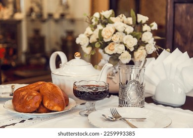 A set table for tea drinking in retro style of USSR times - baked pies, faceted glasses in metal stand, teapot, vase with flowers, napkins with lace. - Powered by Shutterstock