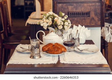 A set table for tea drinking in retro style of USSR times - baked pies, faceted glasses in metal stand, teapot, vase with flowers, napkins with lace. - Powered by Shutterstock