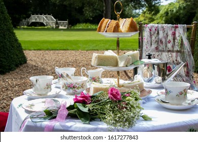Set table for traditional vintage british afternoon tea with cake, sandwiches and view of green garden