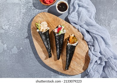 Set of temaki sushi on wooden platter in minimalistic style. Aesthetic composition with handrools on concrete background. Contemporary japanesse cuisine - temaki sushi
