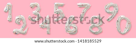 Set of ten Arabic numerals, edible figures made of white royal icing or meringue with colored sugar sprinkles. Top view isolated on pastel pink background. Confectionery decorative design.