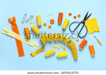 Set of thread spools with measuring tape, scissors, fabric and sewing supplies on blue background