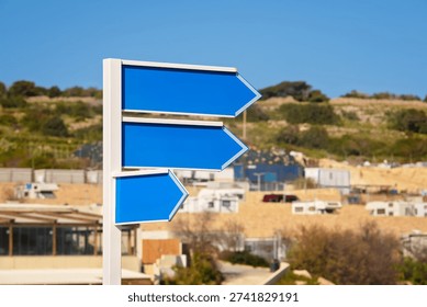 Set of three empty blue arrow signs on white metal pole against defocused sunny beach under clear sky. Space for text, close up.